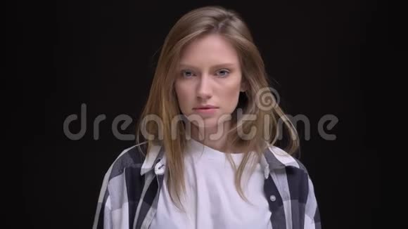 年轻集中的白种人长发女孩的肖像穿着衬衫认真地看着镜头在黑色背景视频的预览图