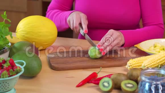 穿着粉红色上衣的女人在桌子上切着多汁的绿色猕猴桃视频的预览图