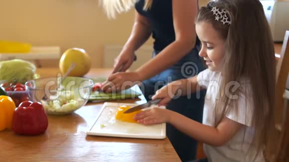 小可爱的女孩正在学习从她妈妈那里切蔬菜女孩仔细地看着重复着视频的预览图