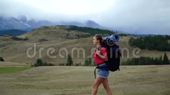 年轻的旅游妇女带着背包走在山路上看着山有很多视频的预览图