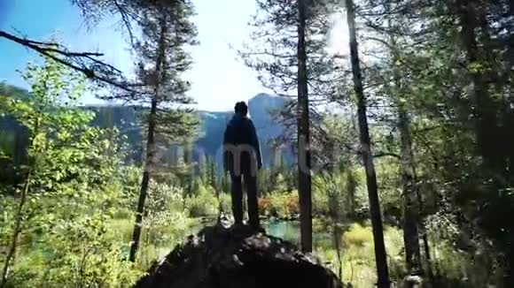 年轻快乐的旅行女孩带着背包和帽子站在山上一个风景如画的蓝色湖泊上把他放在那里视频的预览图