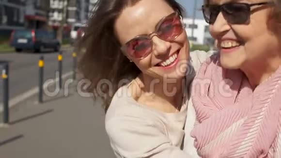 两个女人近照母亲和女儿在城市街道上阳光明媚的日子戴眼镜的女人们欢笑着拥抱着视频的预览图