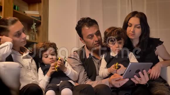 阿拉伯家庭坐在沙发上在舒适的氛围中饶有兴趣地观看客厅里的平板电脑视频的预览图
