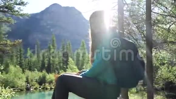 在一个阳光明媚的日子里旅行者女孩坐在背景上美丽的蒙丹湖上的石头上阳光照在女人身上视频的预览图