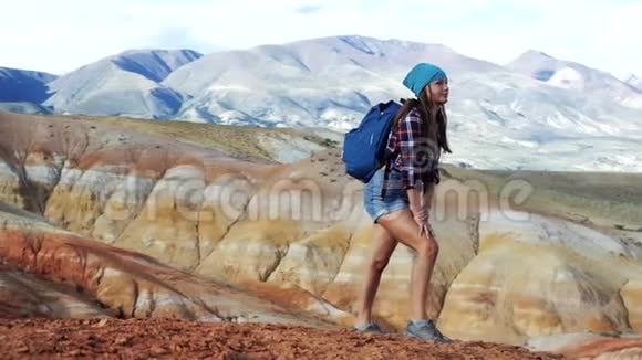 穿着牛仔裤短裤和运动鞋背包的旅行女孩站在一座红山上有不真实的风景视频的预览图