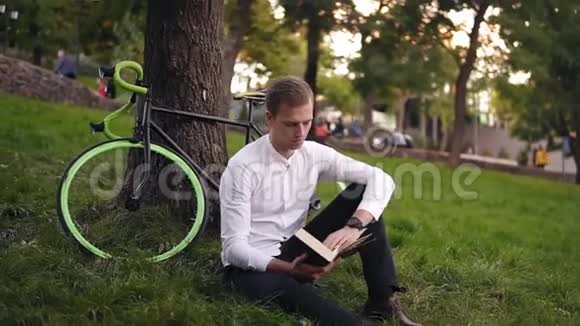 年轻严肃的白种人看书坐在草地上城市公园读书或看书闲暇时间在视频的预览图