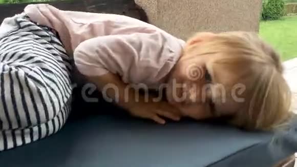 一个笑的金发女孩躺在花园的沙发上视频的预览图