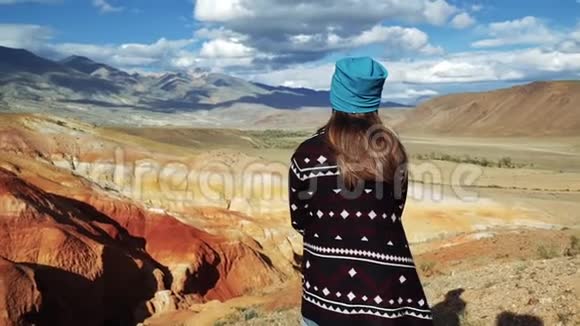 穿着花纹外套的年轻女游客坐在红山的边缘这里风景秀丽天空阴云密布视频的预览图