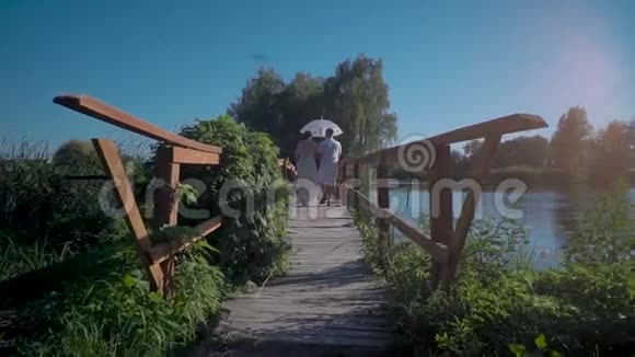 一对相爱的夫妇带着一把白色的伞走在一座木制的乡村桥上视频的预览图