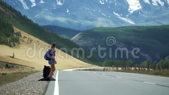 女人搭便车是长期等待汽车和踢背包在山路上那里有雪山视频的预览图