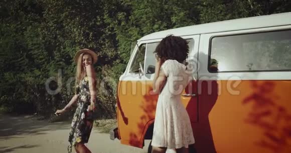 两个漂亮的女孩在老式橙色公共汽车旁的路上拍照快乐地跳舞微笑着穿着靴子视频的预览图