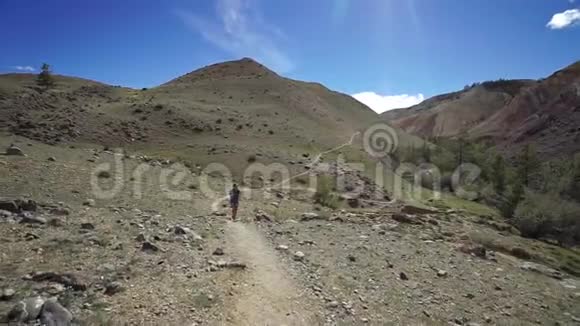 旅行者女孩走在石山上的悬崖小径上背景中有美丽的山和晴朗的天空视频的预览图