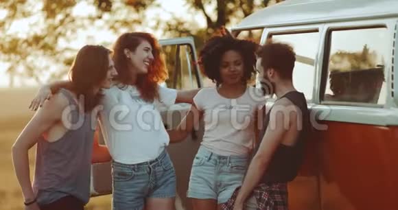 四个多元文化的好朋友在他们的橙色面包车旁的场地中间度过了愉快的时光每个人都拿着视频的预览图