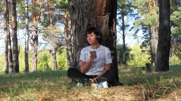 年轻女子坐在公园的一棵树旁休息听音乐有节奏地移动音乐户外娱乐和视频的预览图