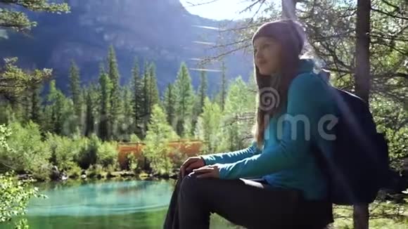 在一个阳光明媚的日子里旅行者女孩坐在石头上望着前方的背景美丽的蒙丹湖视频的预览图