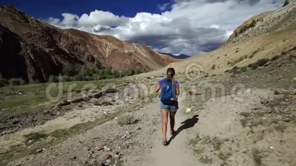 旅行者女孩走在石山上的悬崖小径上4背景中有高山和多云的天空视频的预览图