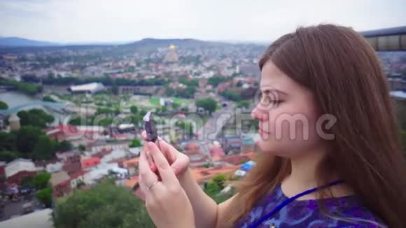 年轻美丽的旅游女孩正在智能手机摄像头上拍摄城市景观微笑着视频的预览图