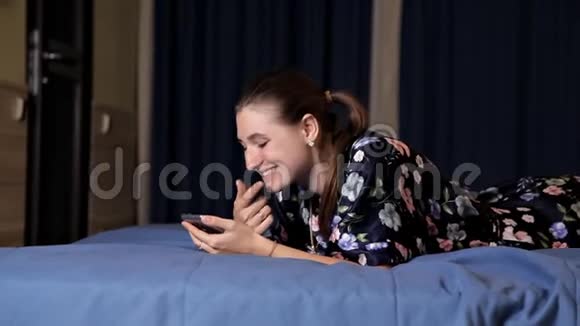 年轻女子使用手机智能手机幸福的女人微笑着躺在卧室的床上视频的预览图