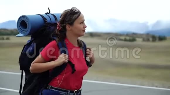 背着背包和太阳镜的旅行女孩站在山路上背景中有雪山视频的预览图