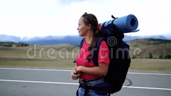 年轻的旅游妇女带着背包和太阳镜在山路上搭便车女孩是从他的手中视频的预览图