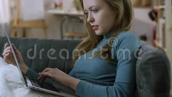 年轻漂亮的女人在沙发上用笔记本发短信视频的预览图