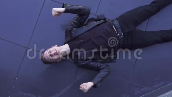 年轻的金发帅哥穿着黑色夹克躺在瓷砖地板上唱歌视频的预览图