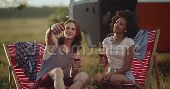 非洲卷发小伙子和她的长发朋友在野餐时在一个美丽的地方拍照视频的预览图