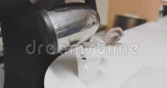 女孩把电热水壶里的开水倒进杯子里视频的预览图