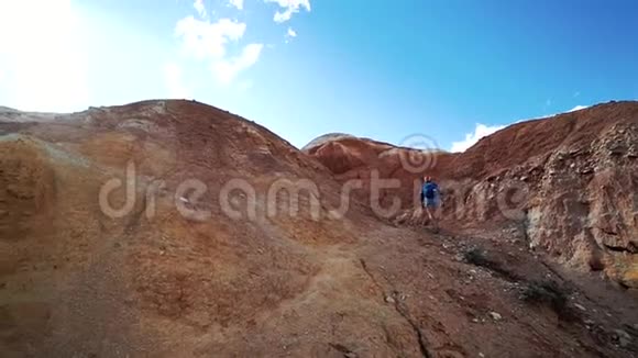 年轻的旅游妇女在阳光明媚的日子里爬上一座红石山背面视频的预览图