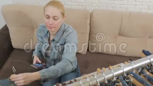 一个女人坐在沙发上用一部智能手机检查和拍照这是一套挂在沙发上的牛仔服装视频的预览图