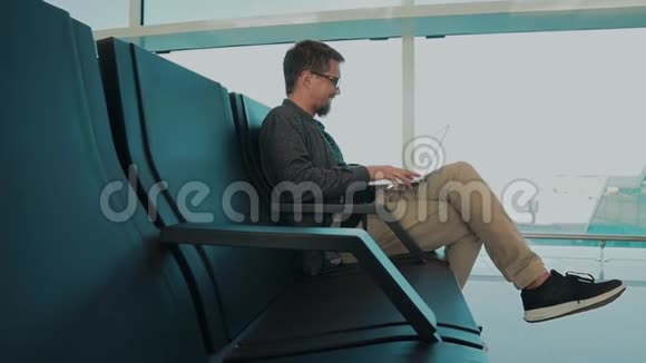 大胡子坐在机场候机楼里用笔记本电脑进行视频通话视频的预览图