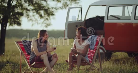 两个种族的朋友一男一女坐在大自然的中央野餐令人惊叹的是喝酒和喝酒视频的预览图