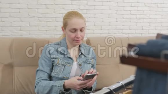 一个女人坐在沙发上用一部智能手机检查和拍照这是一套挂在沙发上的牛仔服装视频的预览图
