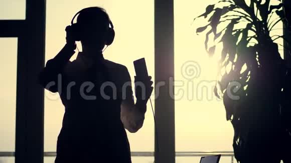 商业女性的黑色轮廓手里拿着耳机和手机跳舞在背景下听音乐视频的预览图