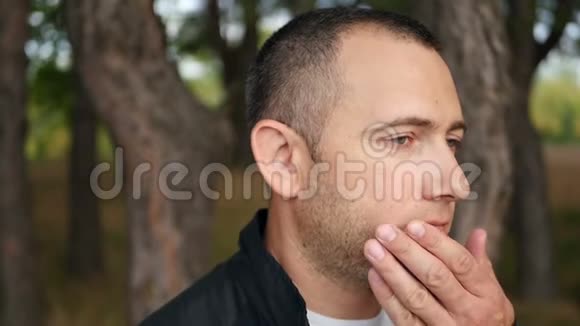 一位沉思的男性游客正站在森林的户外英俊残忍的男人用胡茬触摸他的脸视频的预览图