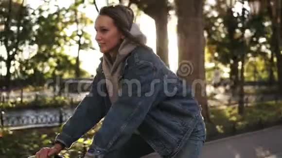在晨间公园或林荫大道上骑自行车的迷人微笑女性的近景年轻人的侧视视频的预览图
