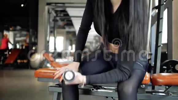 漂亮的身材年轻的白种人女孩坐在长凳上做二头肌锻炼在健身房里举起哑铃视频的预览图