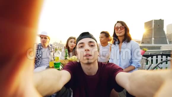 一张照片照片上的年轻人戴着帽子在朋友享受屋顶派对的时候自拍和摆姿势视频的预览图