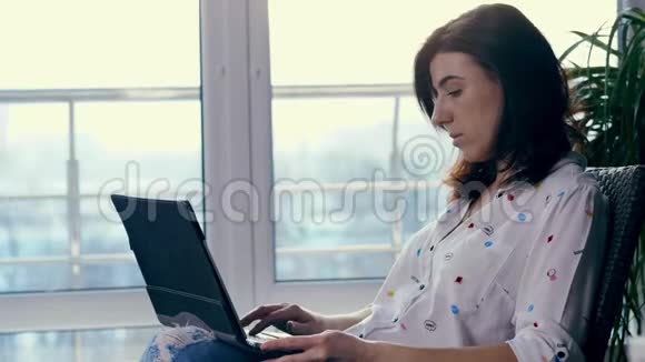 一个年轻的女人一个女孩一个黑发女人穿着白色衬衫和牛仔裤坐在椅子上拿着笔记本电脑3她在网上打字视频的预览图