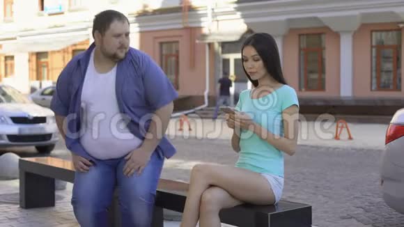 适合美丽的女人无视坐在长凳上的胖子悲伤而不自信的单身汉视频的预览图