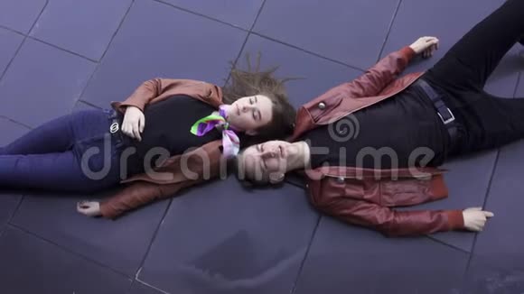 英俊的歌唱青年和可爱的女人躺在黑暗的瓷砖地板上视频的预览图
