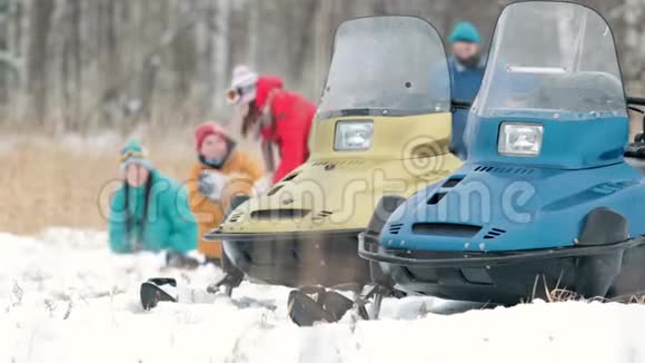 冬天一家人穿着五颜六色的衣服玩雪球前景上的雪地摩托慢动作视频的预览图