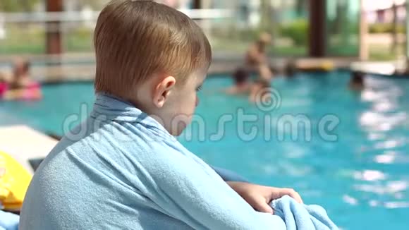 一个小男孩正坐在游泳池旁的一个阳光休息室里用毛巾包着视频的预览图