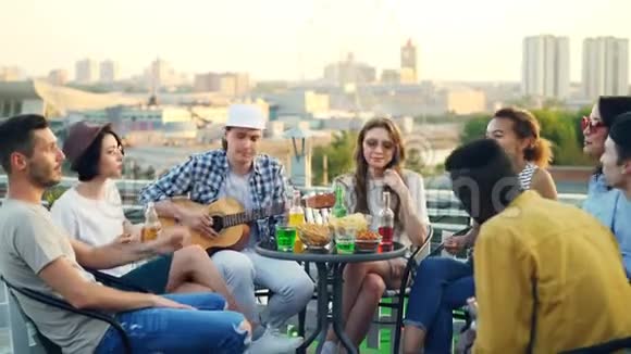 男吉他手在弹吉他而他的朋友们在唱歌笑喝啤酒和软饮料视频的预览图