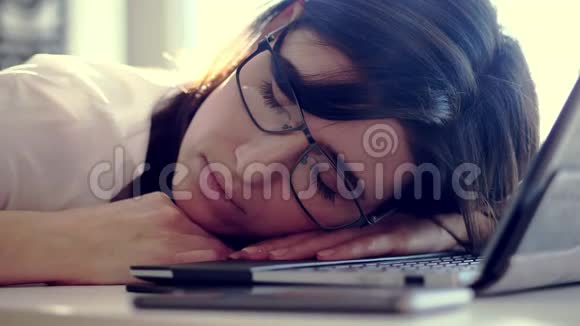 工作过度精疲力竭疲惫不堪的年轻女商人戴着眼镜休息着睡在办公桌上的笔记本电脑上视频的预览图