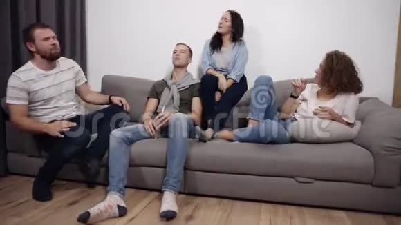 四个有趣的年轻人坐在沙发上唱歌朋友在家客厅享受休闲乐趣视频的预览图