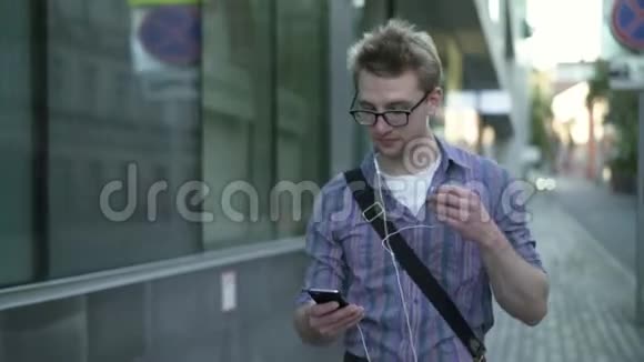 穿条纹衬衫的年轻人走在街上戴着耳机听音乐视频的预览图