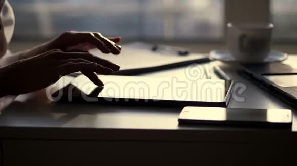 特写女性双手暗影她正在用平板电脑打字接下来是一个杯子手机笔记本电脑视频的预览图