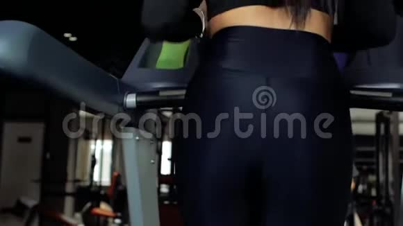 运动的年轻黑发女孩在跑步机上跑步穿黑色上衣和黑色紧身裤的运动女孩背面视图视频的预览图