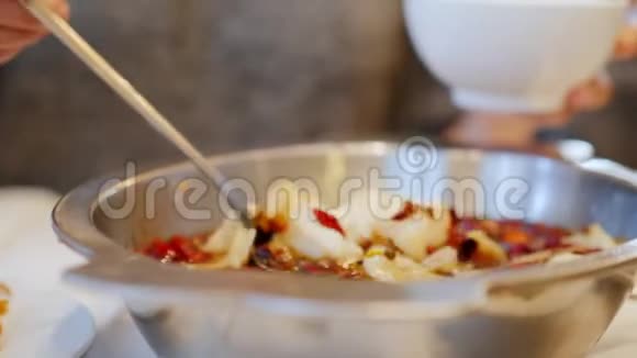 女人把辛辣的海鲜汤倒在他的盘子里鱼片漂浮在加香料的肉汤里正宗中国菜视频的预览图